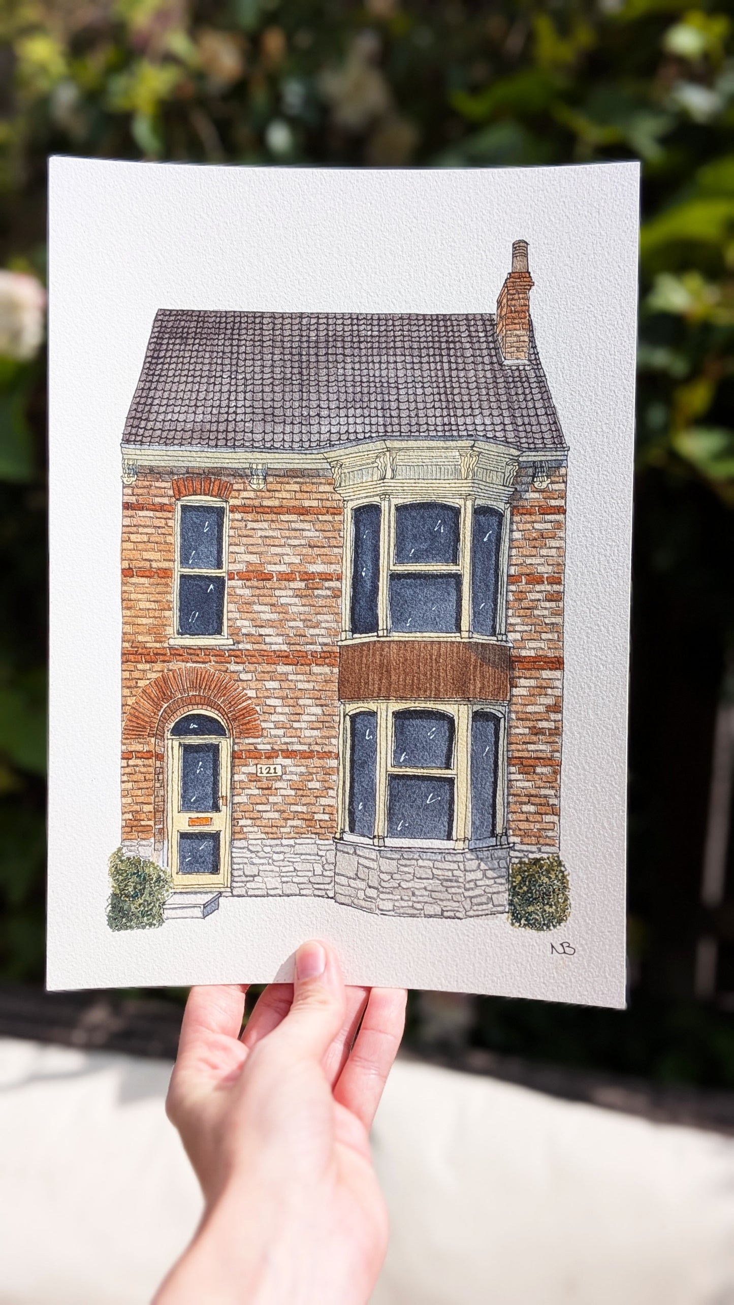 Hand holding a print of a house with a blurred green background