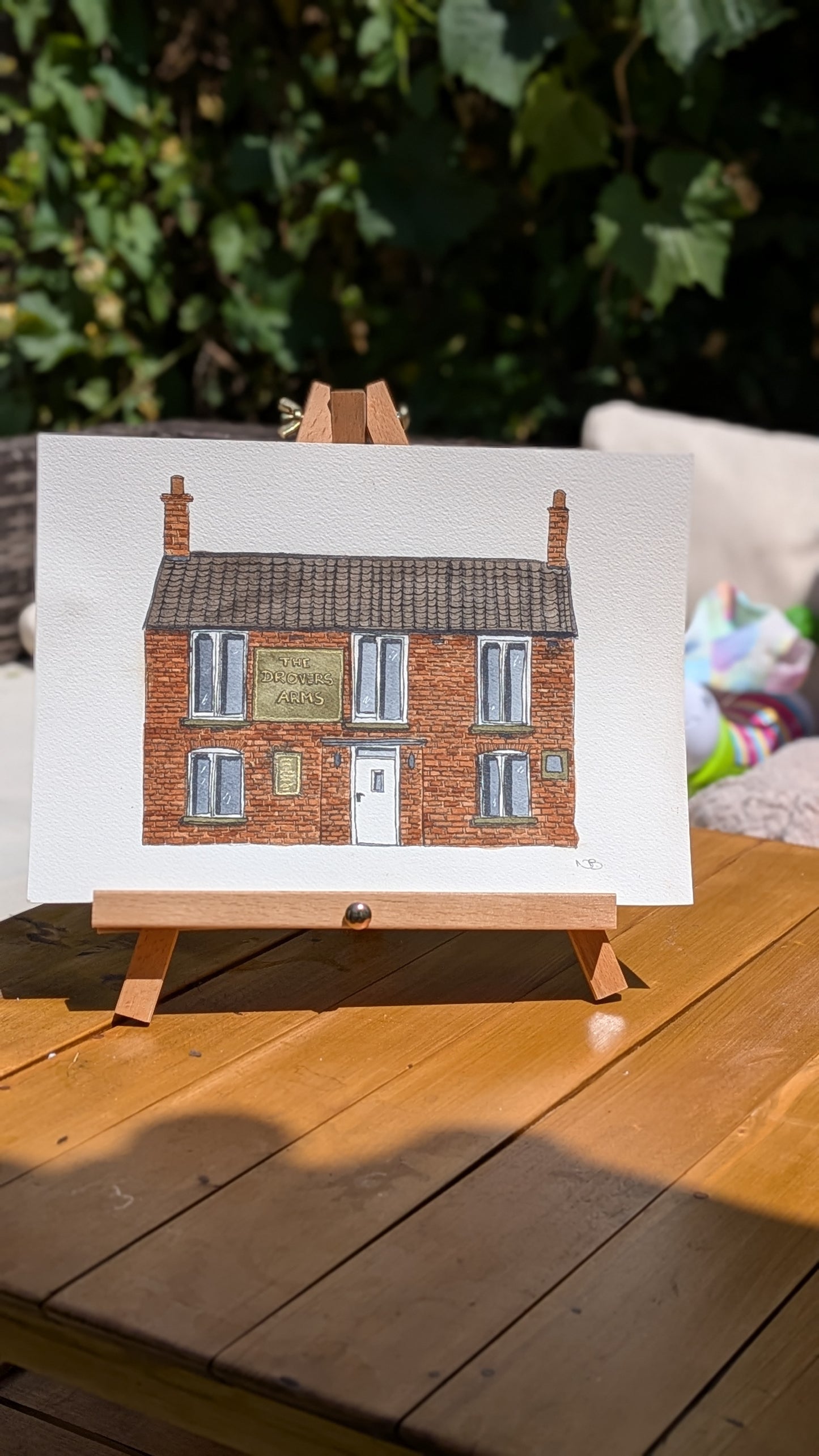 Painting of a brick house on a white canvas with a wooden easel, placed on a wooden surface.
