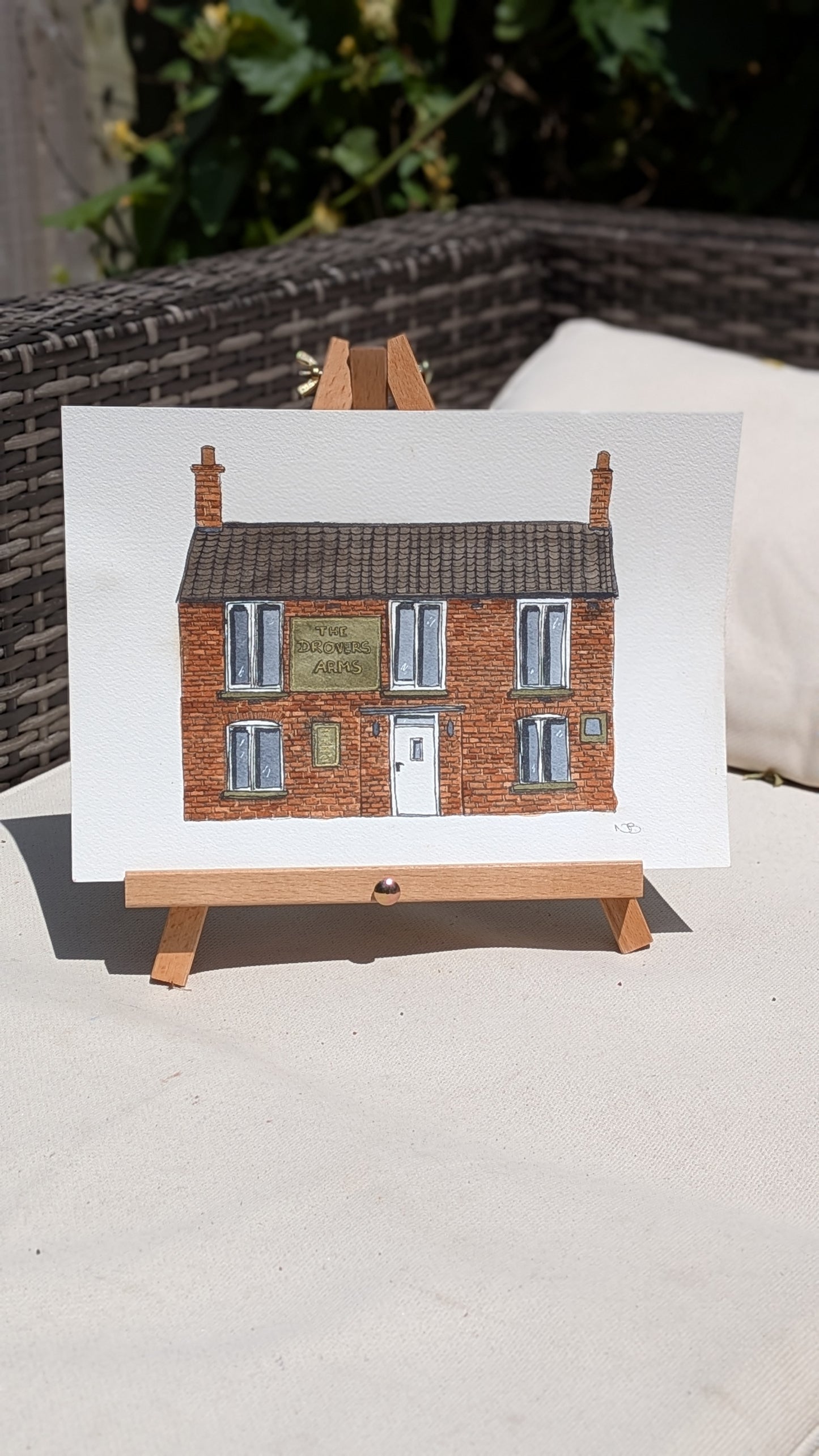 Painting of a house on a white sheet with a wooden easel.