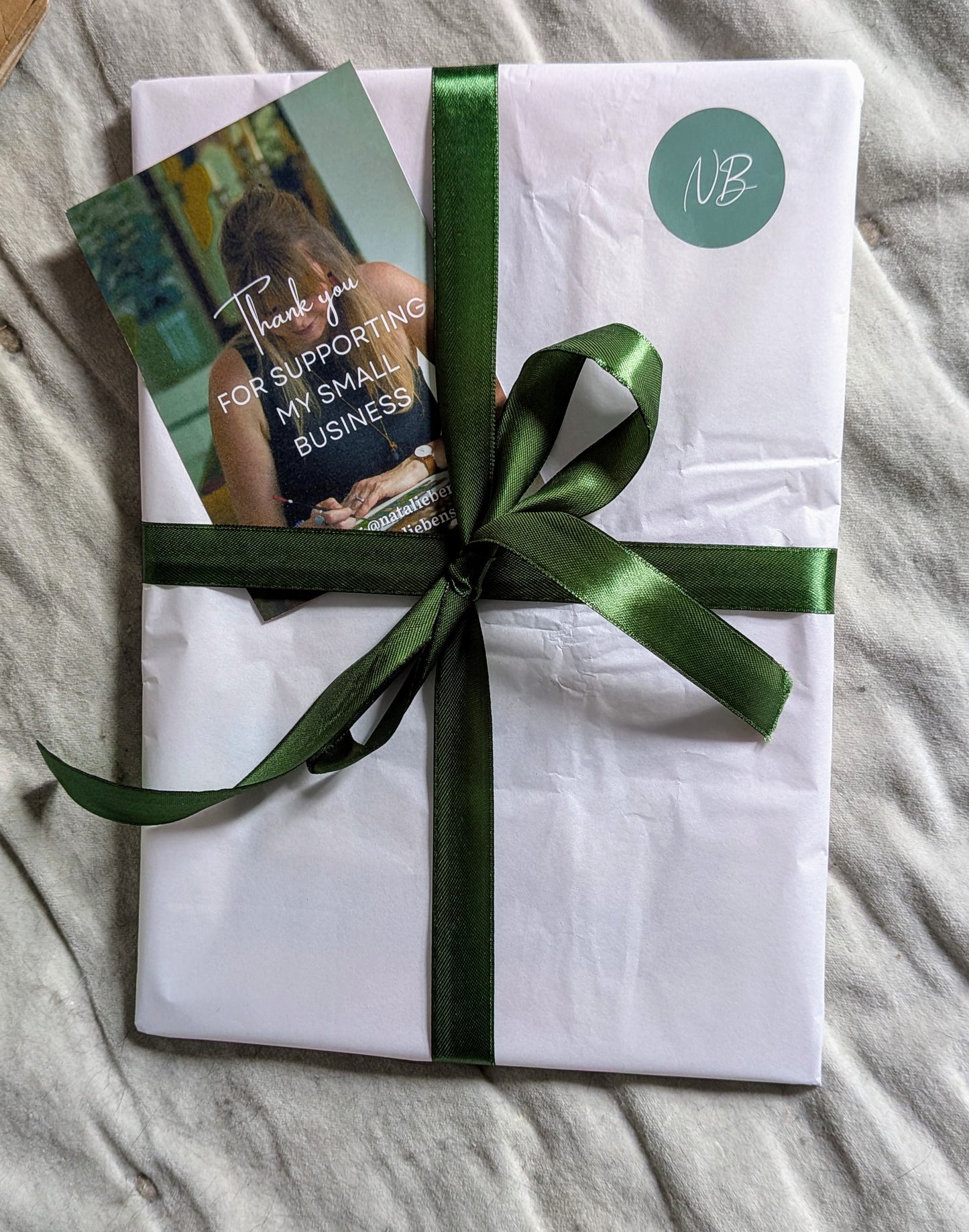 Gift wrapped in white paper with a green ribbon on a gray surface