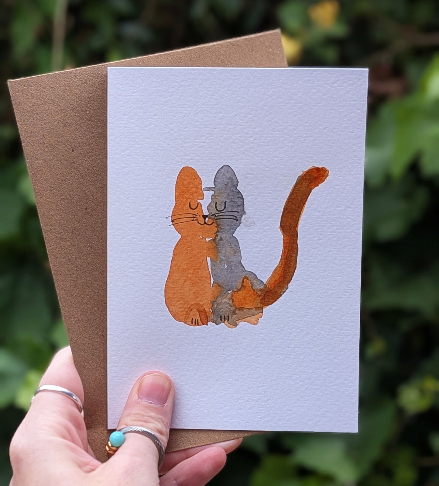 Hand holding a card with a cat illustration against a natural background