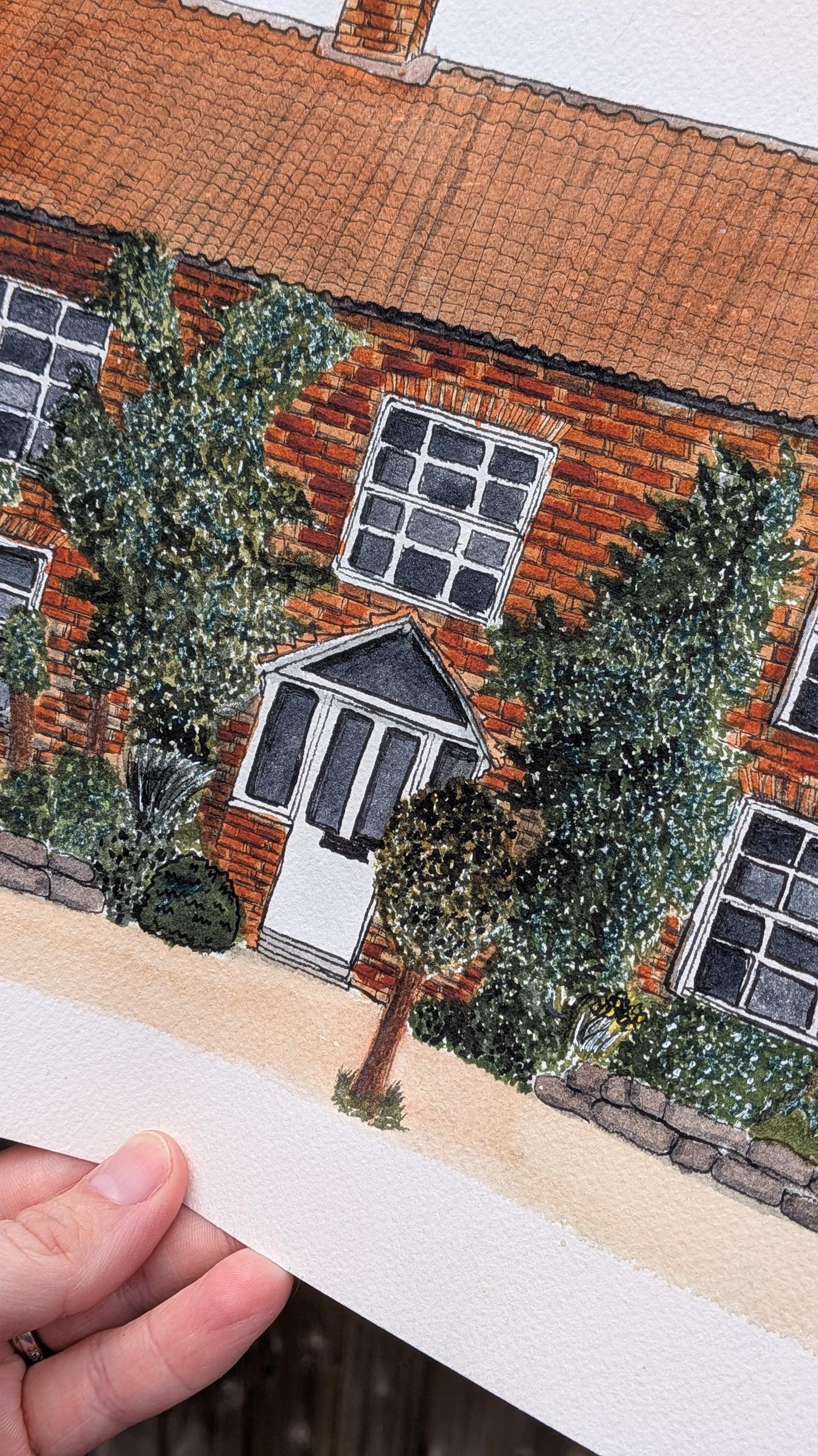 hand holding watercolour painting of a red bricked wedding venue