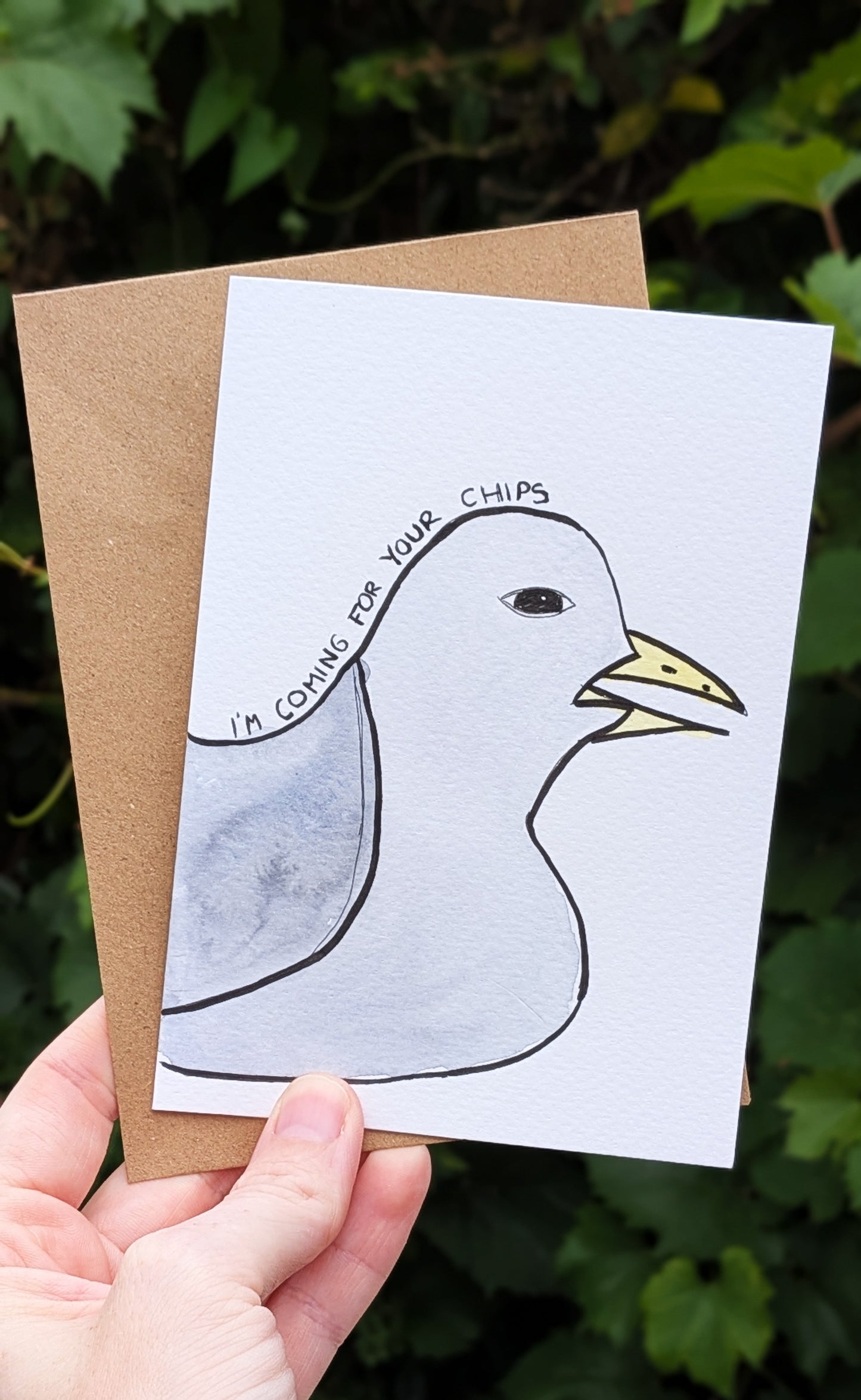 Card with a duck illustration and text held by a hand against a leafy background