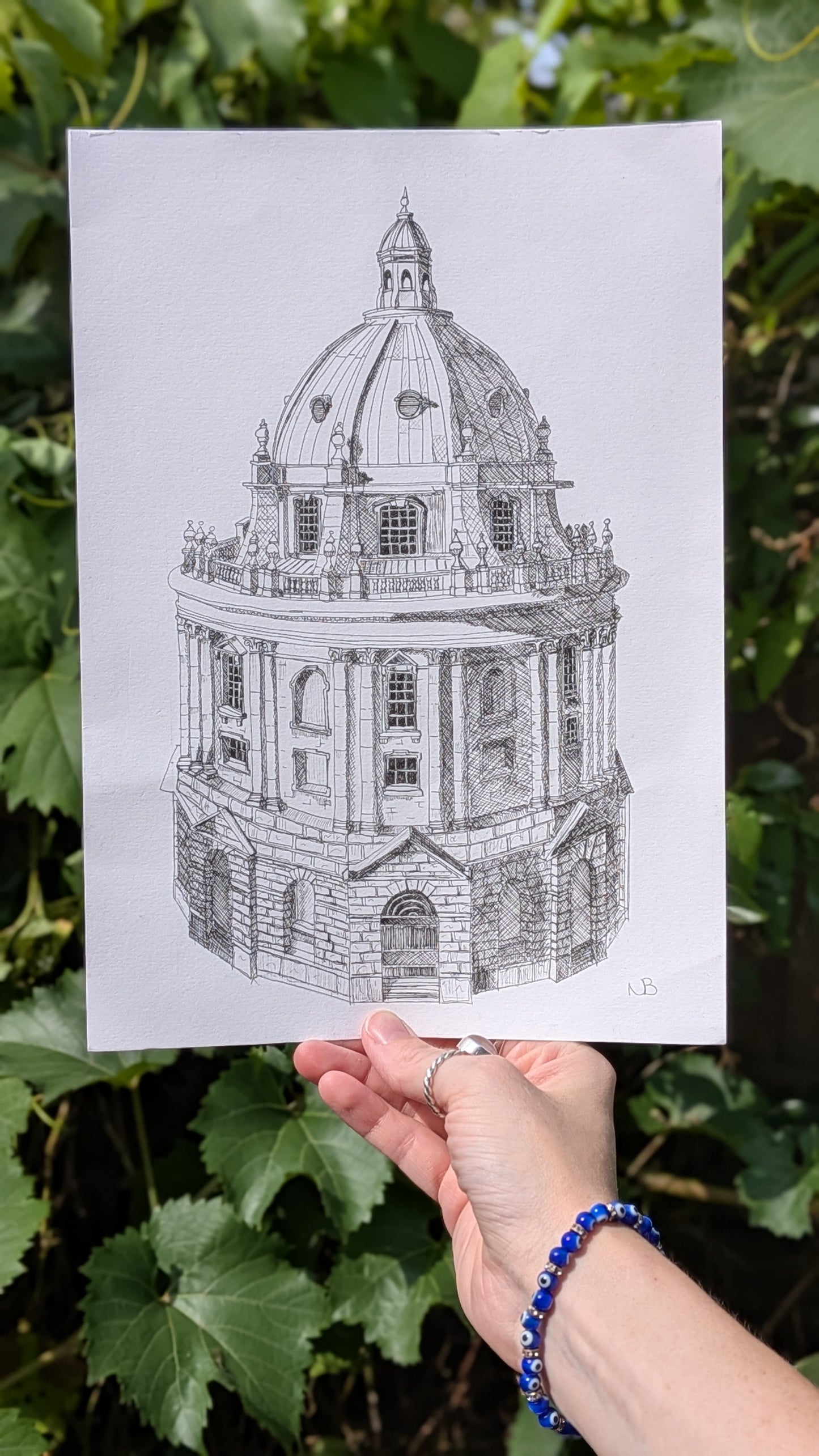 Hand holding a black and white architectural drawing of a dome against a green leafy background