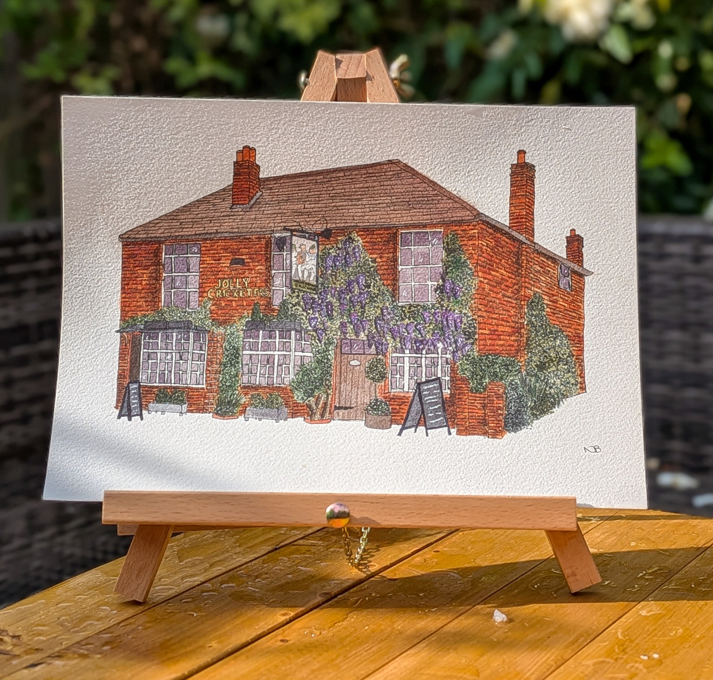 Painting of a brick building with greenery on an easel outdoors.