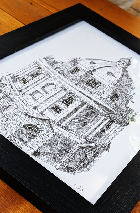 Framed black and white architectural drawing of a building on a wooden surface
