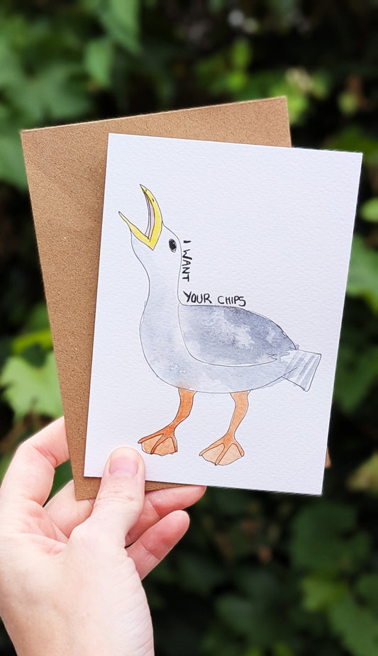 Hand holding a card with a seagull illustration and text, against a natural background.