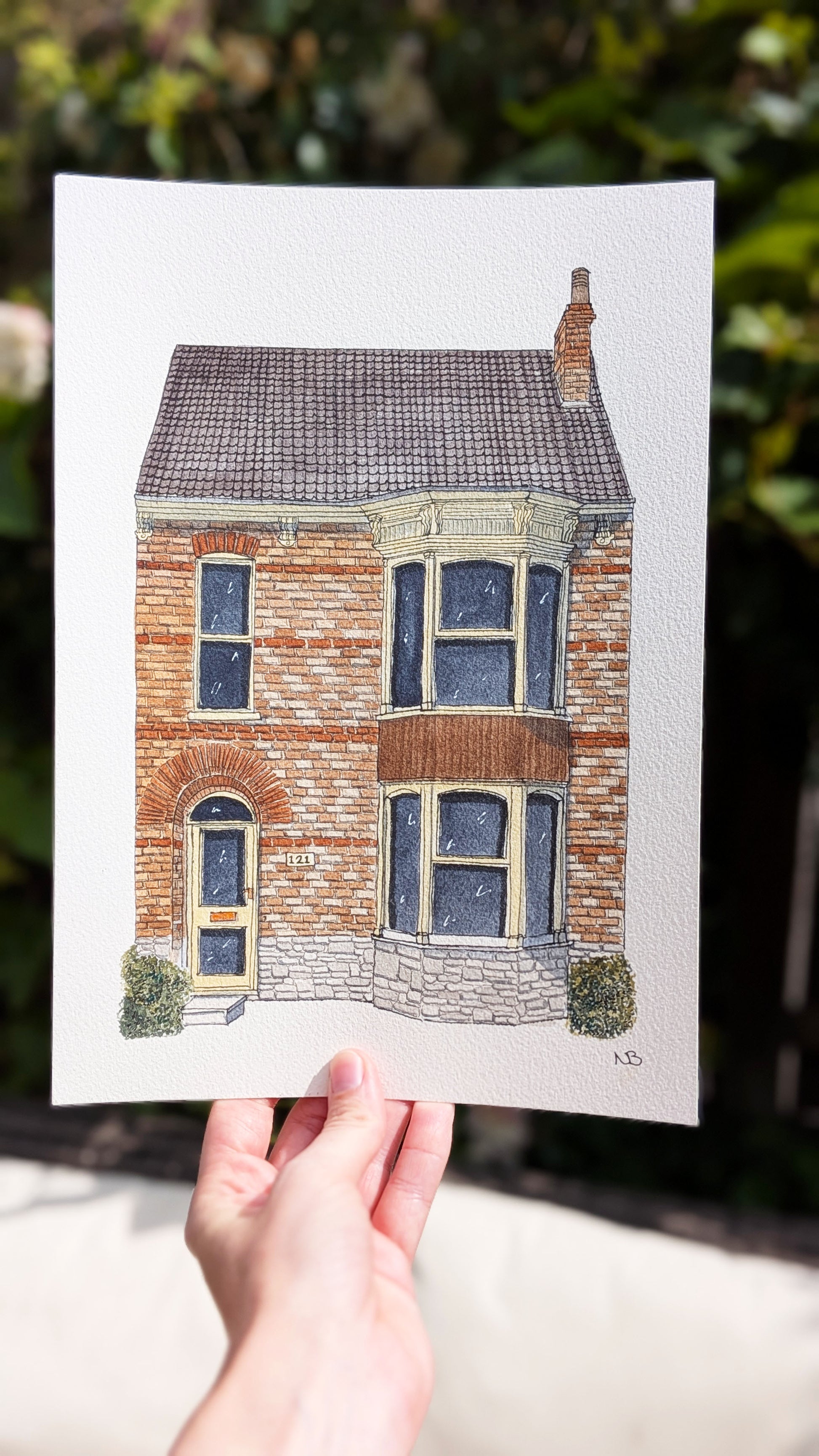 Hand holding a print of a house with a blurred green background