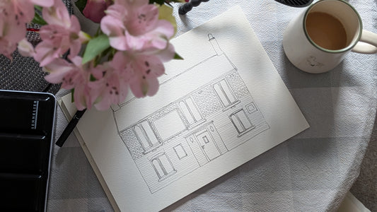 Sketchbook with architectural drawing, pink flowers, and a cup of coffee on a checkered tablecloth.