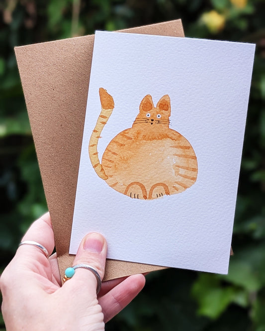 Card with a cat illustration held by a hand against a blurred green background