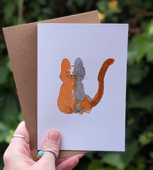 Hand holding a card with a cat illustration against a natural background