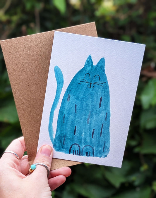 Hand holding a card with a blue cat illustration against a natural background