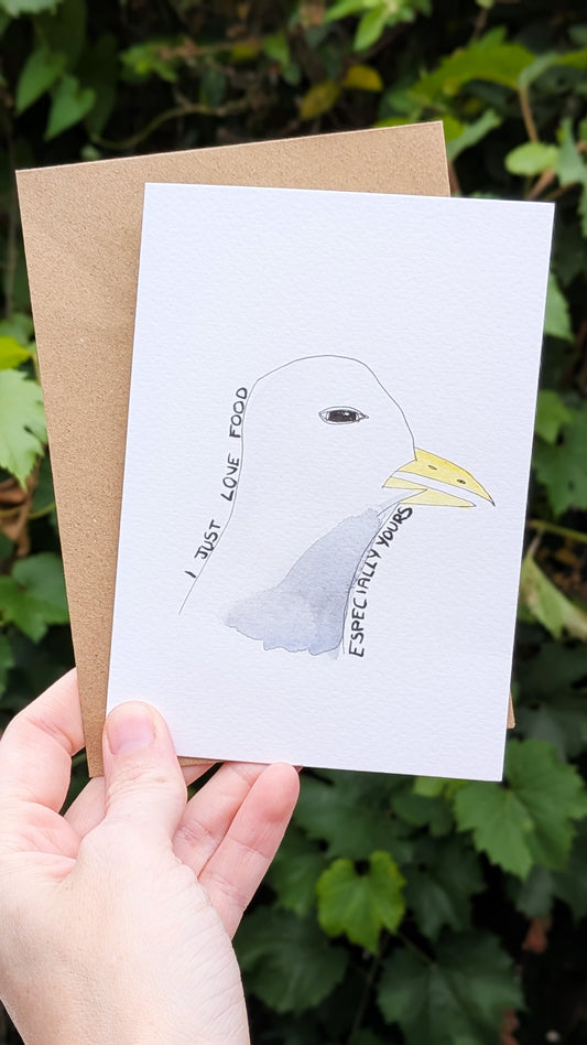 Hand holding a card with a seagull illustration and text against a green leafy background