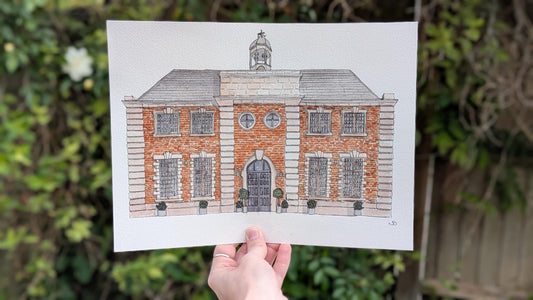 hand holding a watercolour painting of a large red brick wedding venue