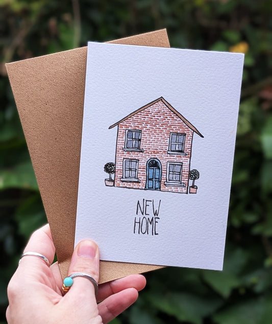 Card with a house illustration and 'New Home' text held by a hand against a blurred green background
