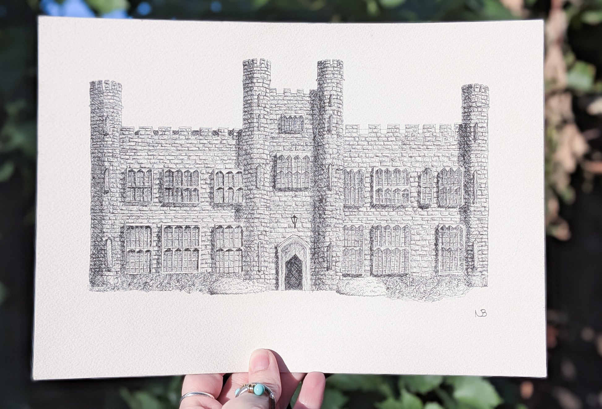 Hand-drawn illustration of a castle held against a natural background