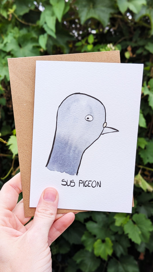 Card with a pigeon illustration labeled 'Sus Pigeon' held by a hand against a green leafy background