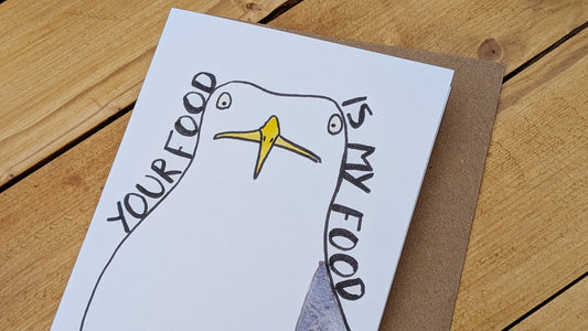 Card with a seagull illustration and text 'Your food is my food' on a wooden surface